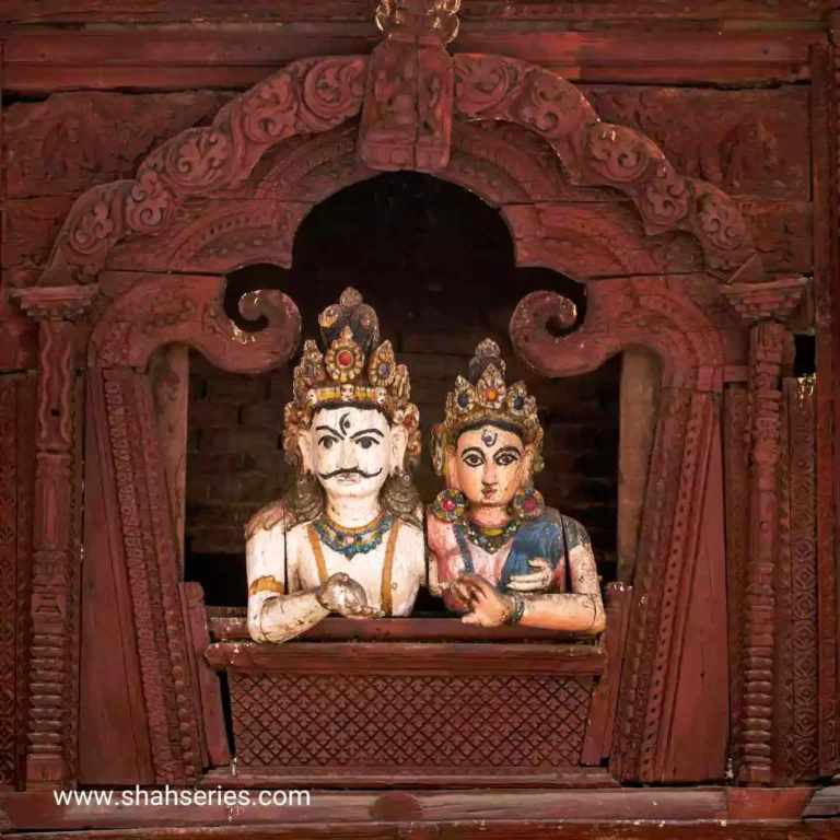 The photo is of a couple of shiv parvati in a doorway. They are located in a temple or building. They are sitting and made of wood.