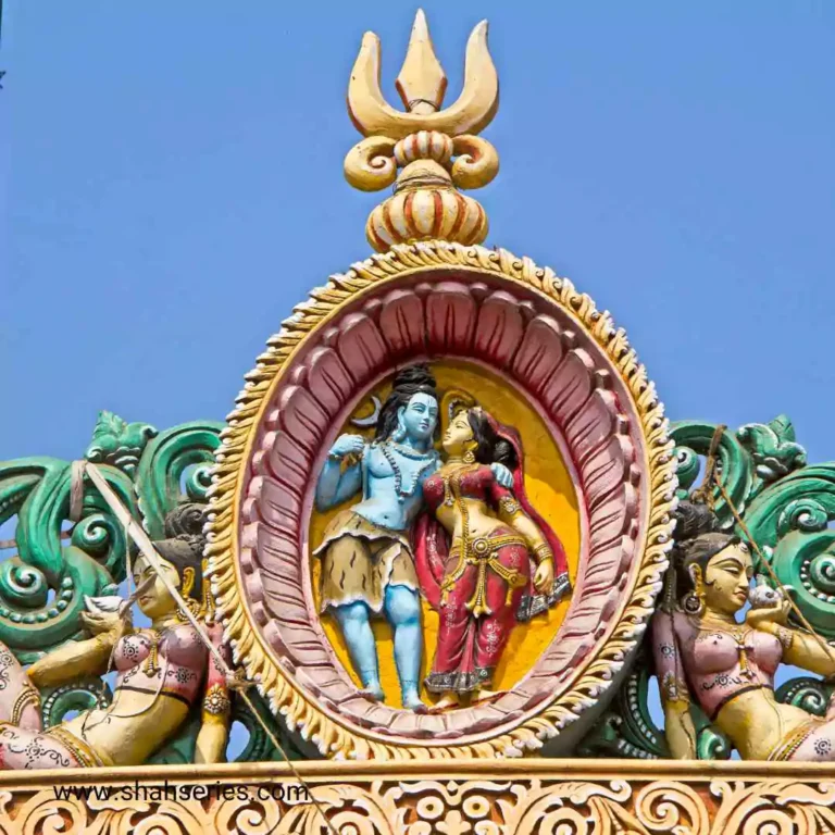 The photo is of a colorful building with Lord Shiva and Goddess Parvati on top. It is an outdoor Hindu temple, with intricate carvings and gold accents. The building is a place of worship and is situated under a blue sky.